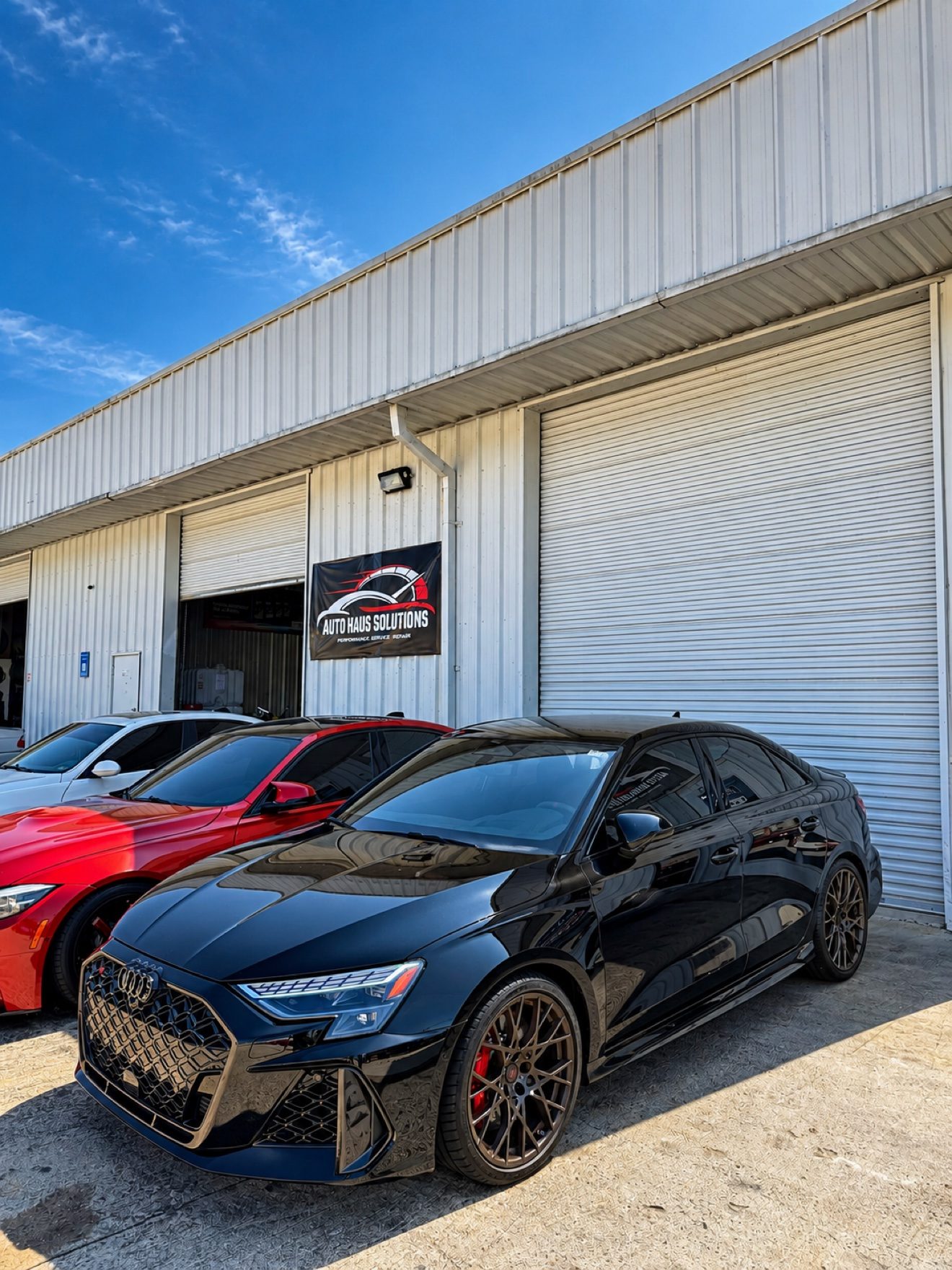 Black Audi RS3 sedan in front of the Auto Haus Solutions shop