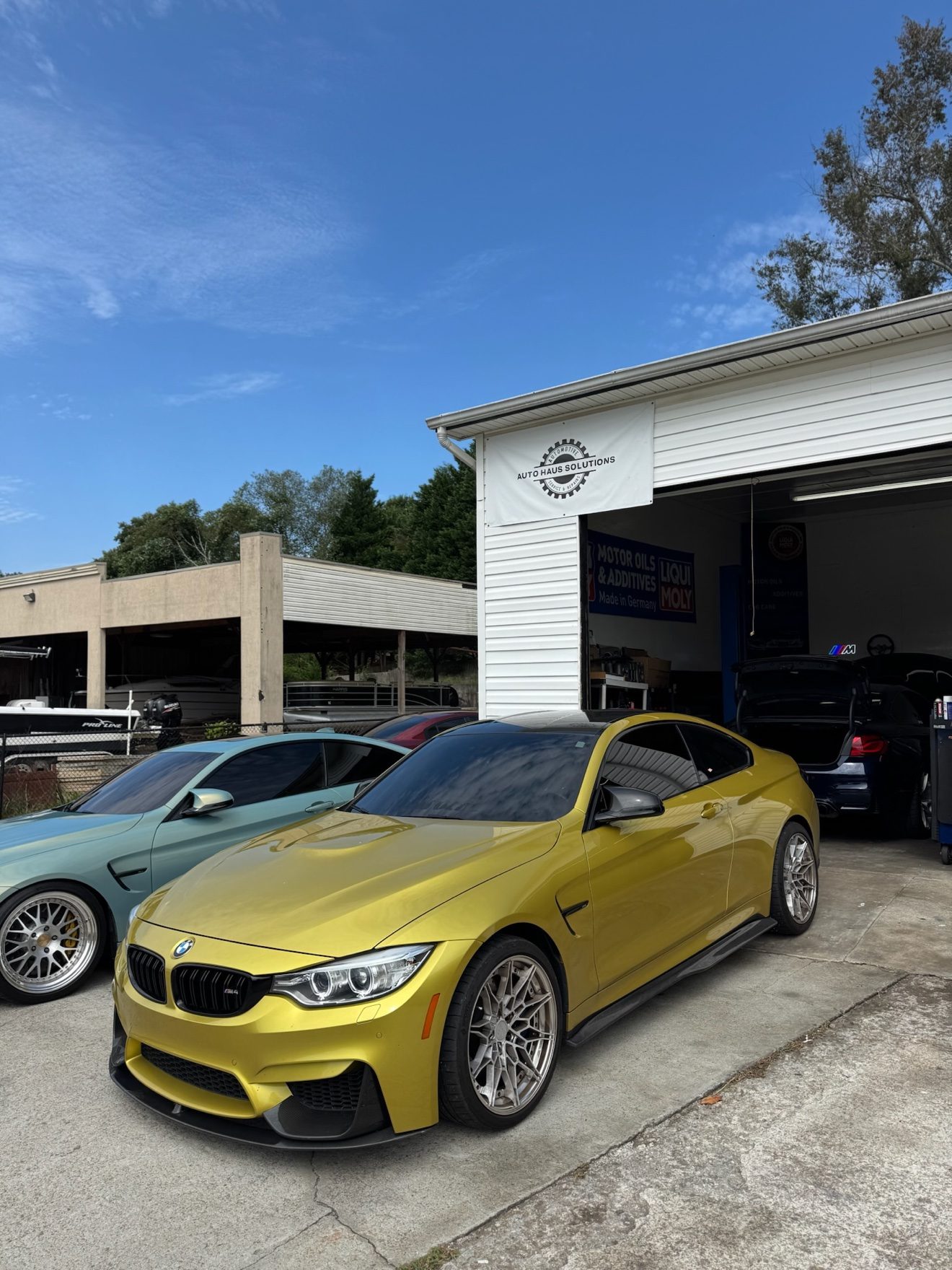 Yellow and teal BMW M4 coupes parked at Auto Haus Solutions