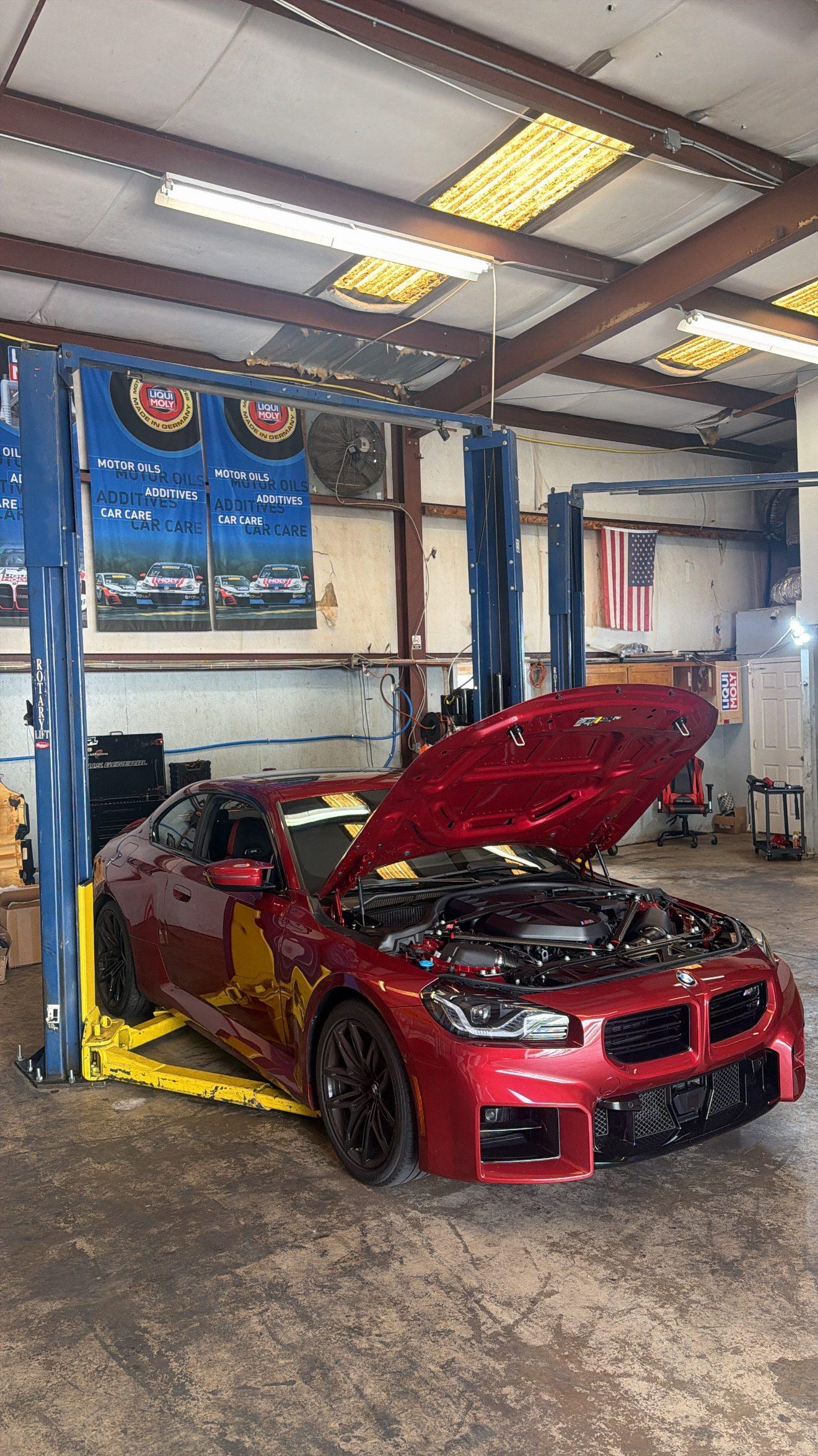 Red BMW M2 coupe on a lift with hood open inside the Auto Haus Solutions service bay